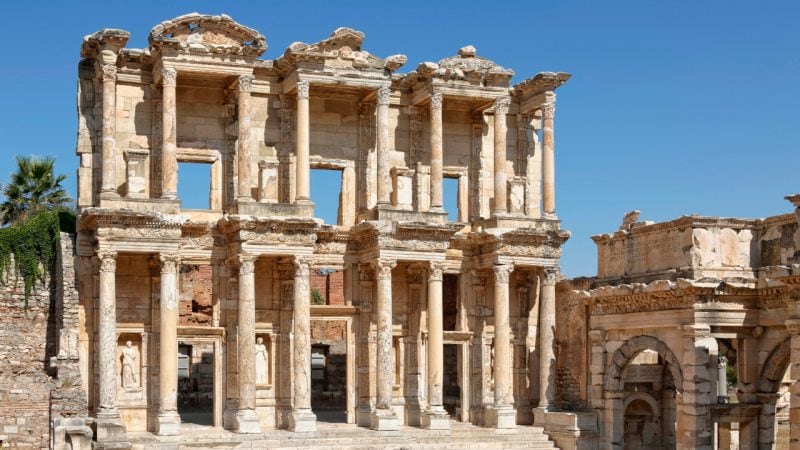 The restored stone facade of the Library of Celsus in Ephesus, featuring two levels of columns and alcoves with statues.