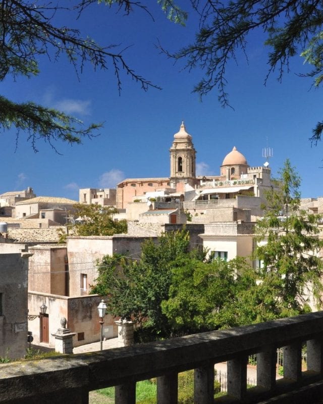 View of a town with stone buildings and a church with a bell tower and dome under a clear blue sky.