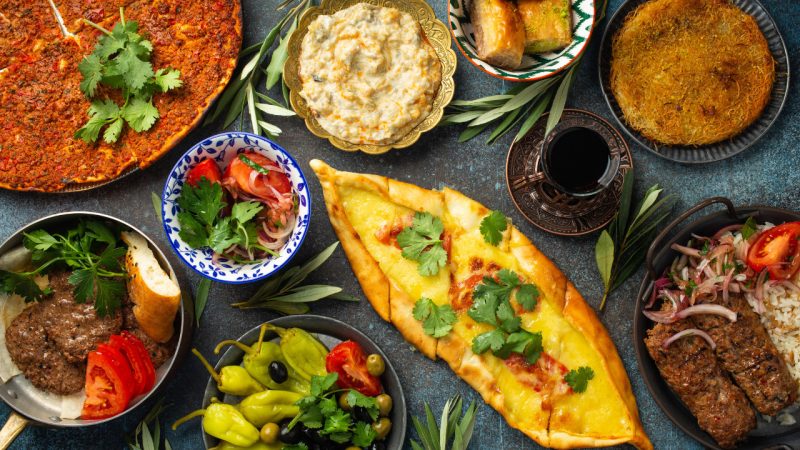 A spread of Turkish cuisine, including lahmacun, cheese pide, kebab, dips, a small salad, baklava, and a glass of tea.