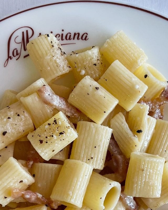 Rigatoni pasta with pieces of guanciale and black pepper on a plate labeled La Matriciana.