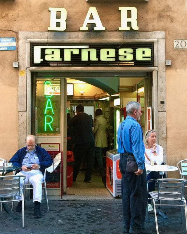 The entrance to Bar Farnese, with a man sitting at an outdoor table and another standing near the doorway.