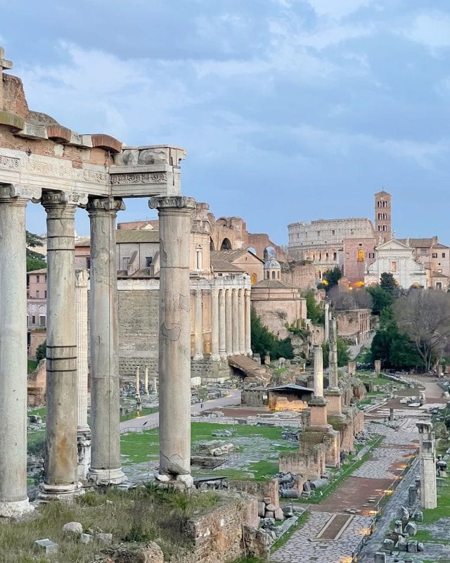 The Roman Forum with ancient stone columns in the foreground and the Colosseum in the distance.