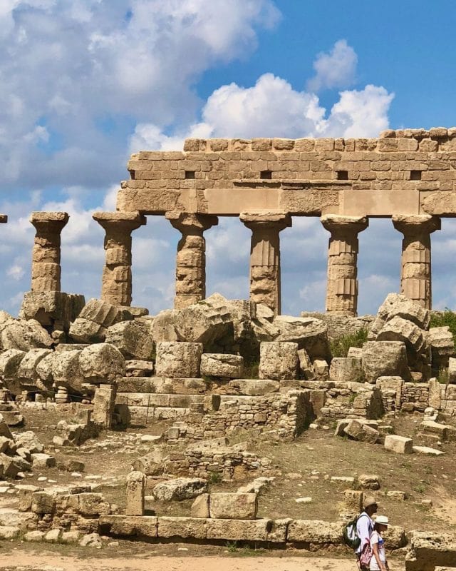 Ancient Greek temple ruins with a colonnade standing above piles of stone rubble.