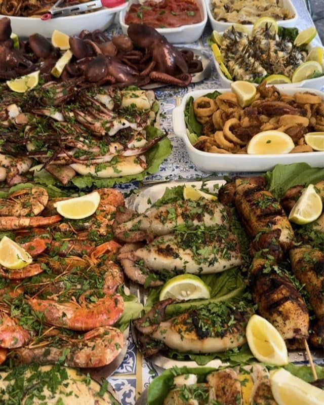 A spread of grilled seafood including octopus, squid, and shrimp, garnished with fresh herbs and lemon wedges.