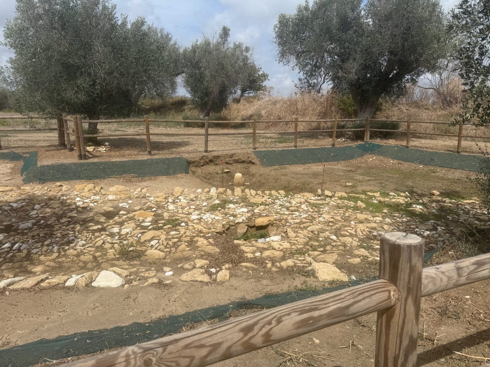 An archaeological excavation site with exposed stone foundations and a wooden fence.