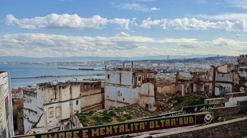 Ruined buildings overlooking the bay and skyline of Algiers, with a painted wall in the foreground.