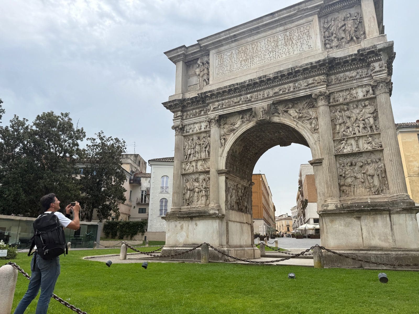 A man with a backpack takes a photo of the Arch of Trajan in Ancona, Italy.