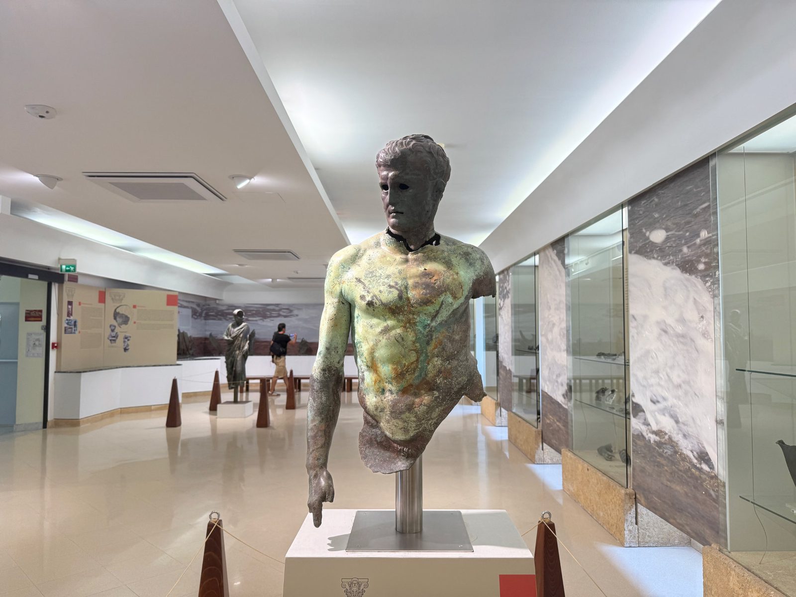 Bronze statue of a male torso on display in a museum.