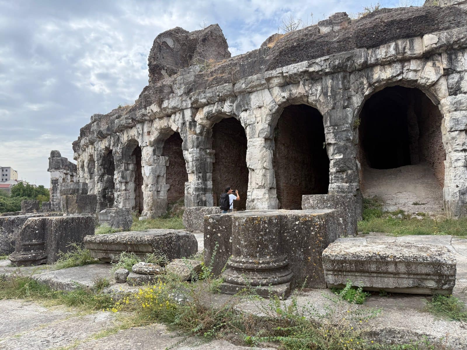 A person taking a photo of the stone arches and ruins of an ancient amphitheater.