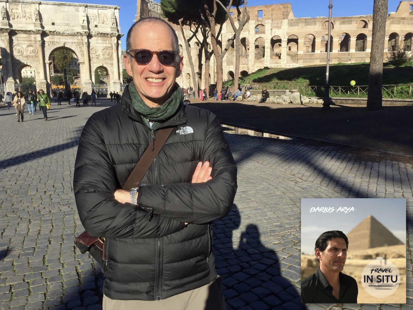 A man wearing sunglasses and a black jacket stands in front of the Colosseum and Arch of Constantine in Rome. An inset shows a podcast cover titled “Travel In Situ” with a man and a pyramid.