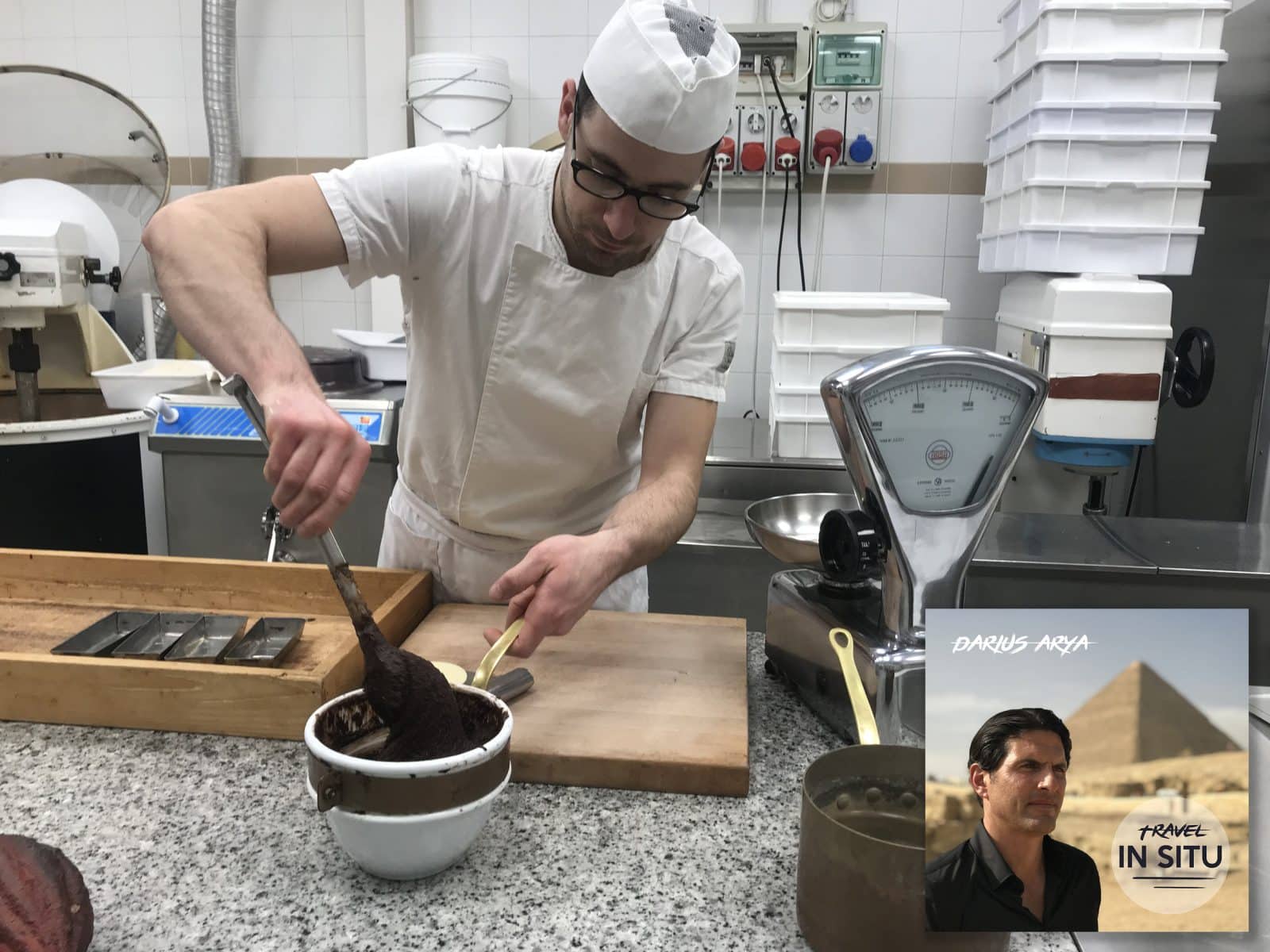 A pastry chef in a white uniform prepares chocolate in a kitchen. Inset: a “Travel In Situ” promo with a man and a pyramid in the background.