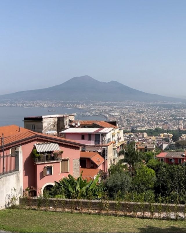 View of a coastal city and Mount Vesuvius from a hillside with residential buildings in the foreground.