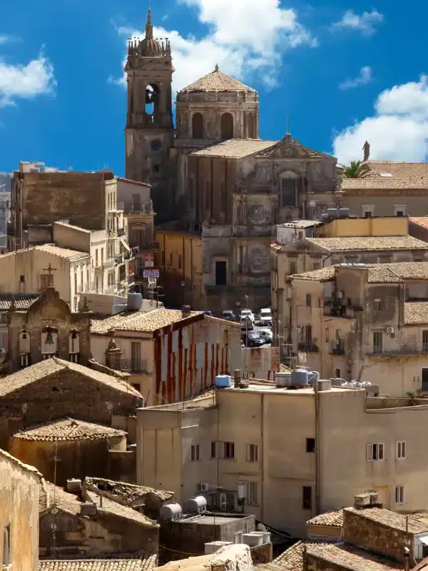 Historic cityscape with stone buildings and a large cathedral under a blue sky with clouds.