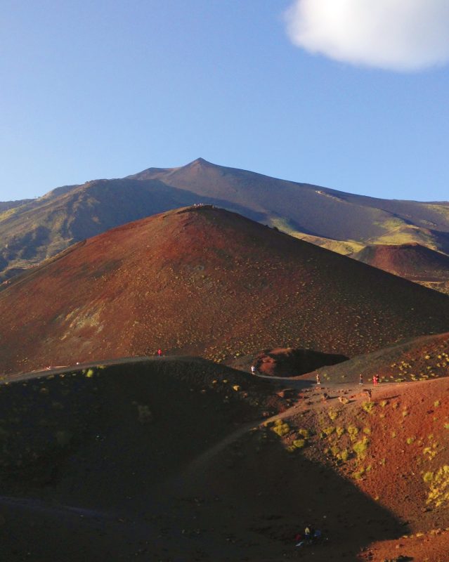 Hikers on the dark red volcanic slopes of Mount Etna.