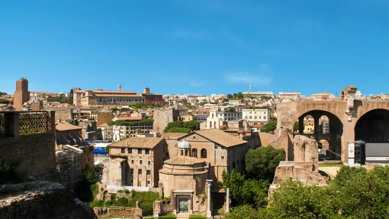 View of ancient ruins and historic buildings under a clear blue sky in a cityscape, with greenery interspersed among the structures.