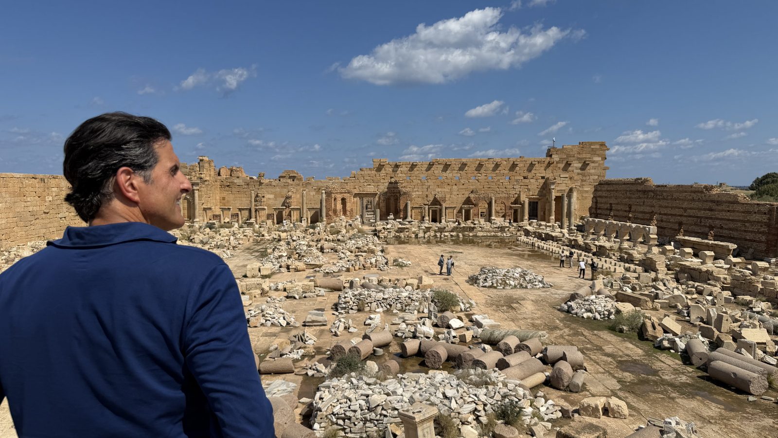 A man in a blue shirt looks out over the ruins of an ancient stone complex.