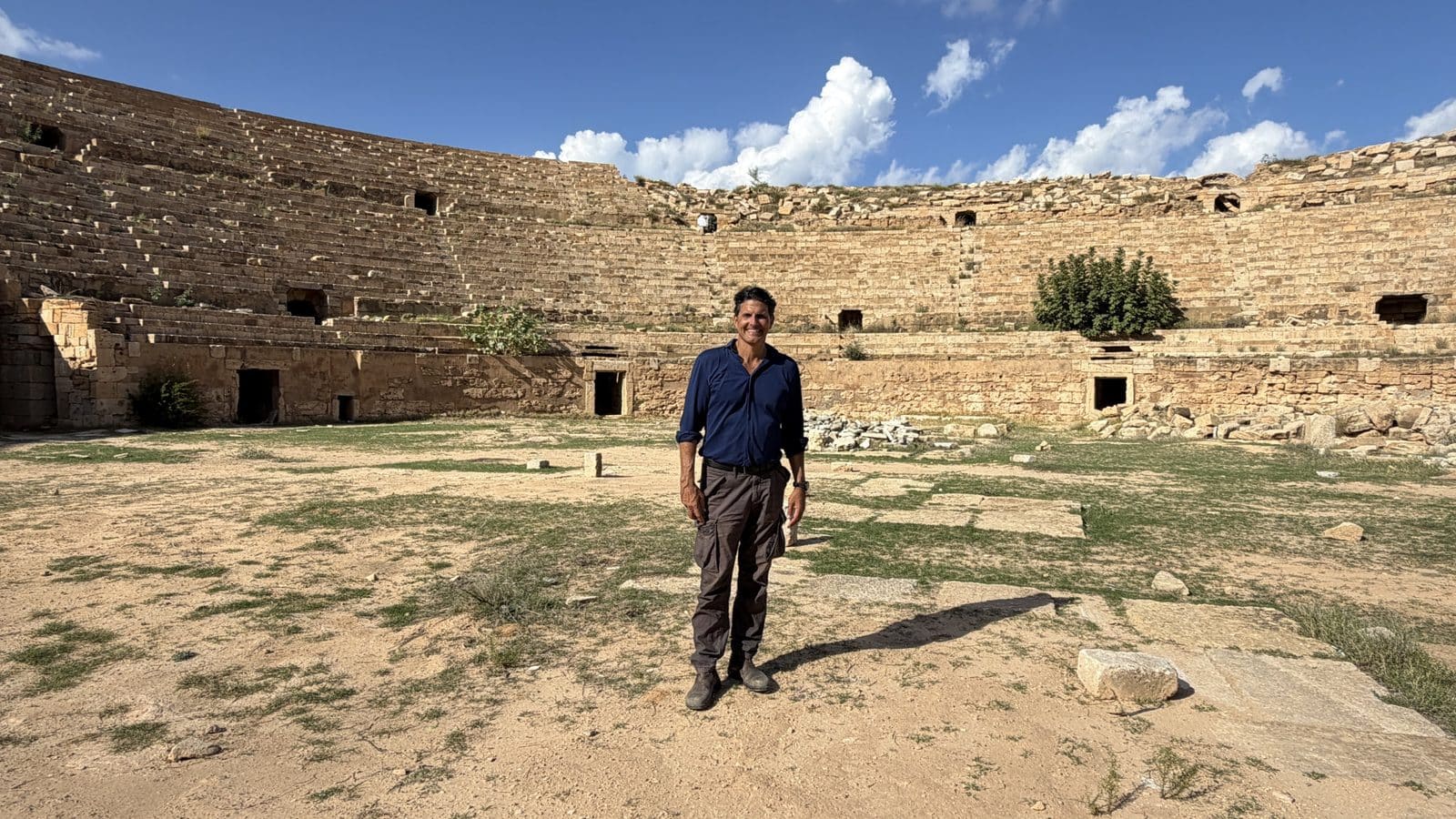 A man stands in the center of an ancient Roman amphitheater.