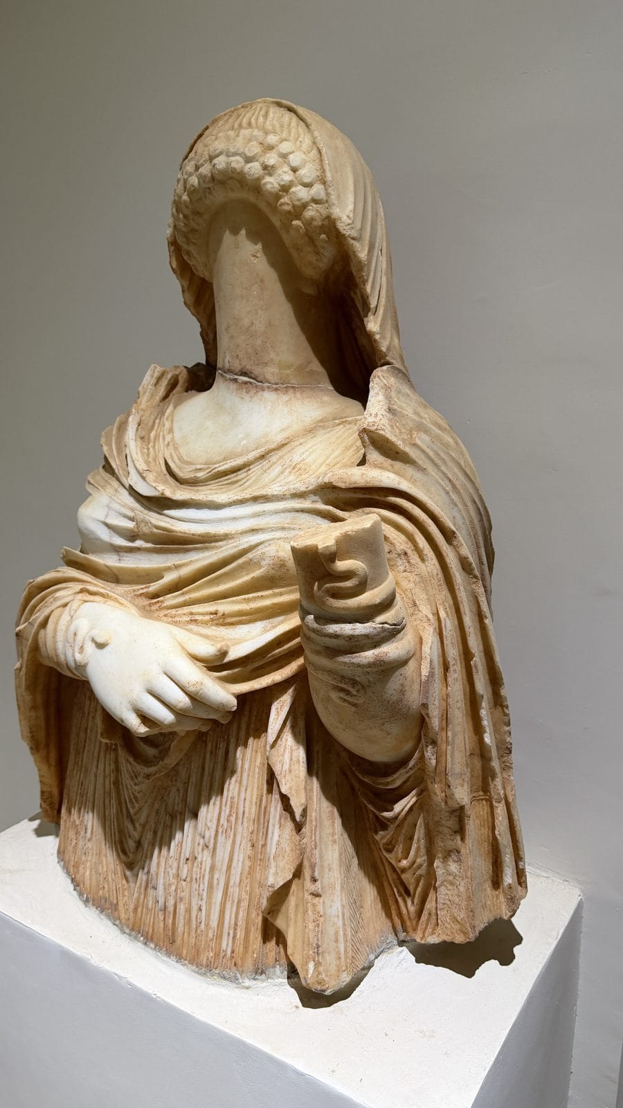 A headless marble bust of a draped female figure holding a small snake.