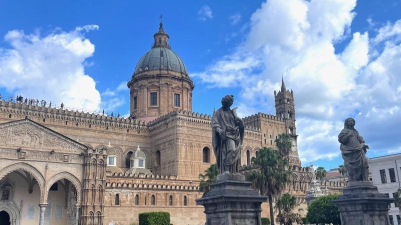 Palermo Cathedral with its large central dome, featuring stone statues in the foreground.