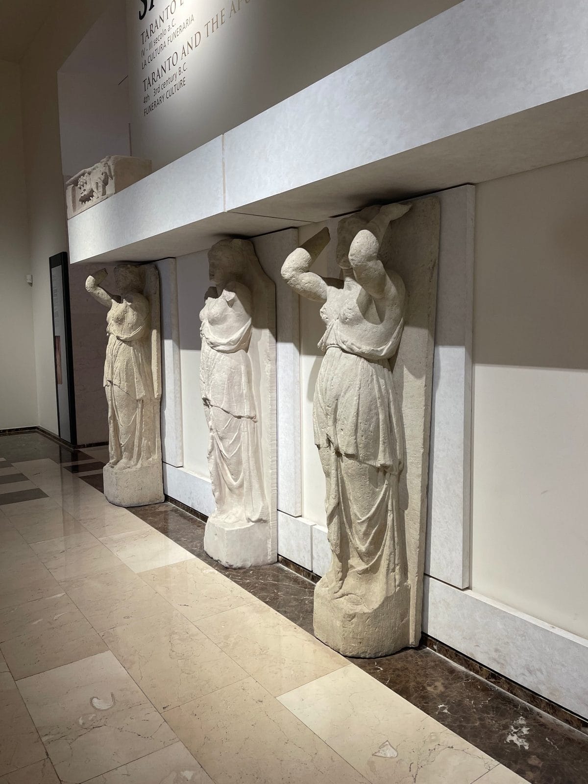 Three stone statues of women acting as architectural columns, displayed against a wall in a museum.