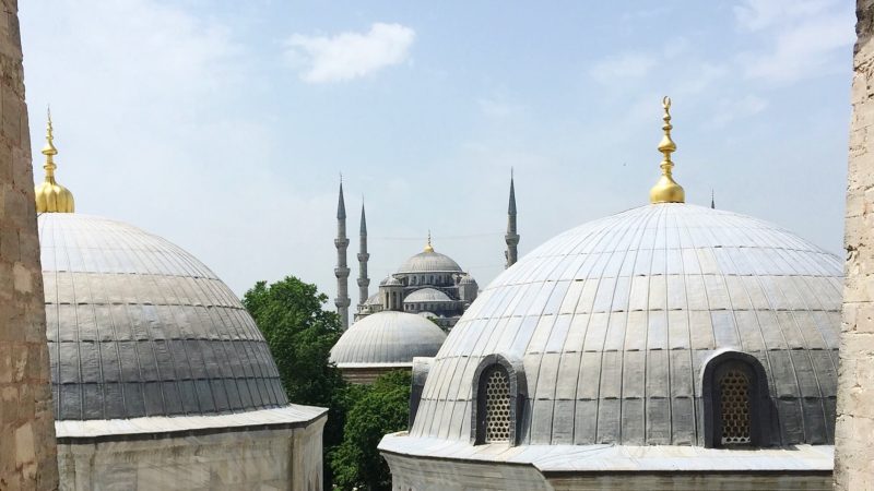 View of the Blue Mosque and its minarets framed by the domes of another structure.