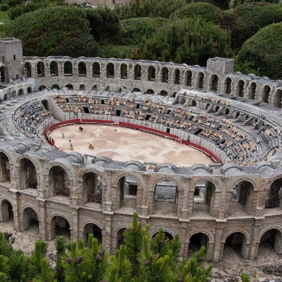 A miniature model of a Roman-style stone amphitheater with rows of tiny figures in the stands and a dirt arena.
