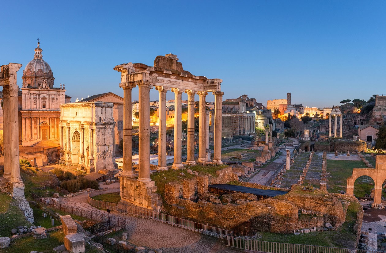 Ancient Roman Forum ruins with standing columns and historic buildings at sunset in Rome, Italy.