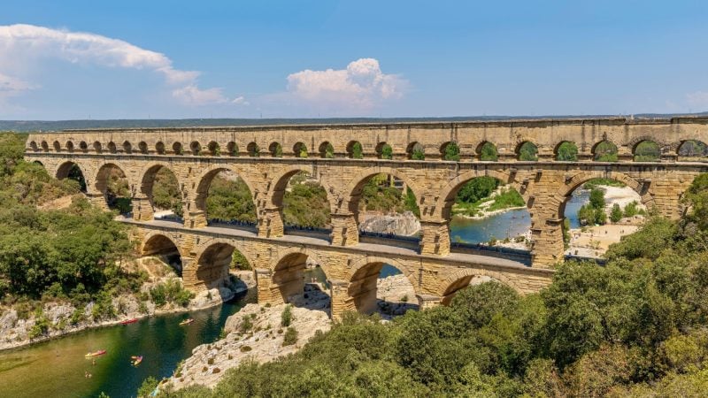 The Pont du Gard aqueduct spanning a river with people swimming and kayaking below.