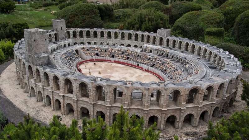 A miniature model of a Roman-style stone amphitheater with rows of tiny figures in the stands and a dirt arena.