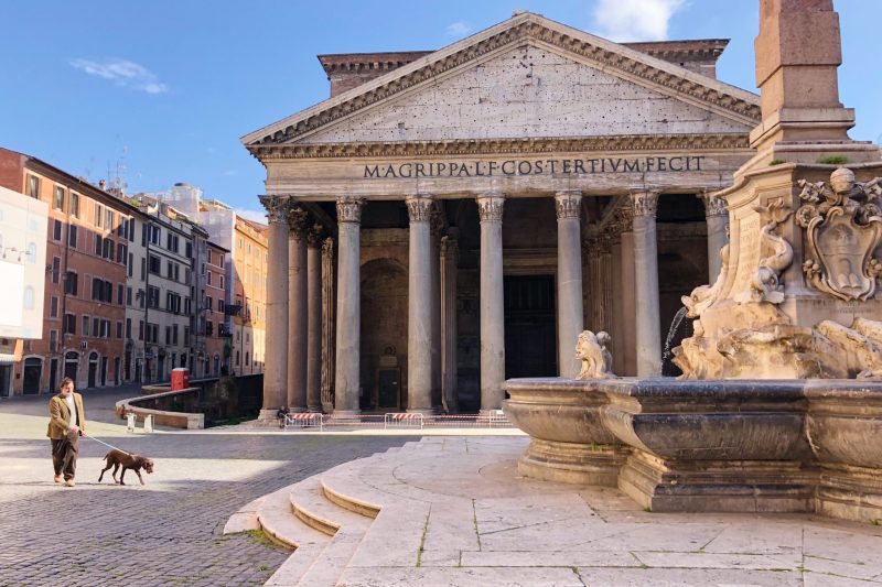 The Pantheon in Rome with a person walking a dog in the foreground near the Fontana del Pantheon.