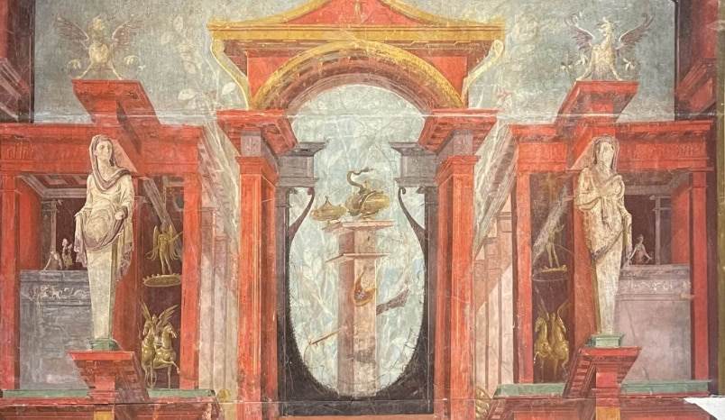 Ancient Roman fresco with red architectural elements, statues of draped figures, and a central pedestal featuring swans and a golden vessel, surrounded by decorative mythological motifs.